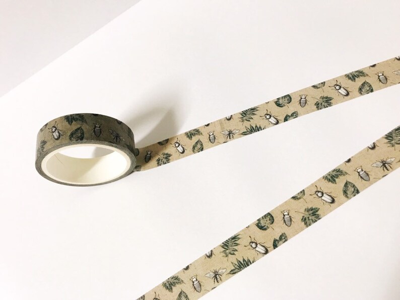 May include: A roll of brown washi tape with a repeating pattern of green leaves and black and white beetles.