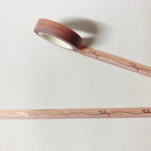 May include: Pink washi tape with gold lettering that says "Today" repeatedly. The tape is rolled up and partially unrolled.
