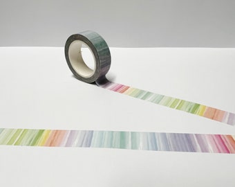 May include: A roll of washi tape with a watercolour rainbow stripe design. The tape is green and has a white core.