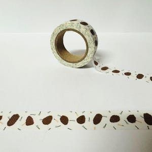 Könnte beinhalten: Eine Rolle weißes Washi-Tape mit einem braunen Tannenzapfenmuster. Das Band ist teilweise abgewickelt und zeigt das Design.
