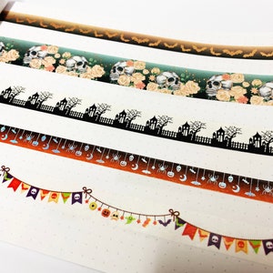 Op de afbeelding: Halloween-thema washi tape rollen. Ontwerpen omvatten vleermuizen, schedels met rozen, spookhuizen, spinnen, manen en feestelijke banners in oranje, zwart en groen. Perfect voor knutselen en scrapbooking.