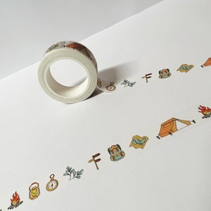 May include: A roll of white washi tape with a camping theme. The tape features illustrations of tents, campfires, compasses, backpacks, and trees.