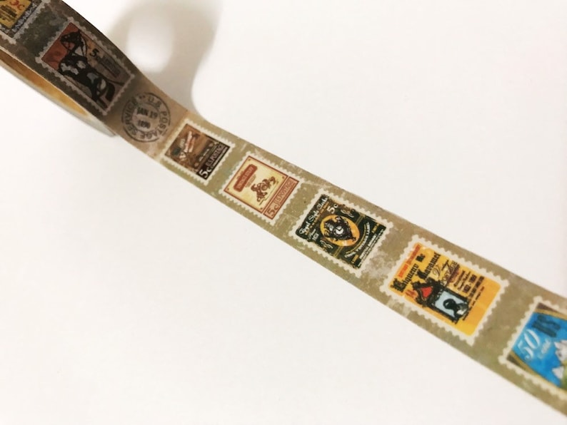 May include: Decorative washi tape featuring a repeating pattern of vintage postage stamps. The stamps have a distressed, aged appearance with various designs and colors, including brown, yellow, and blue. The tape is on a white background.