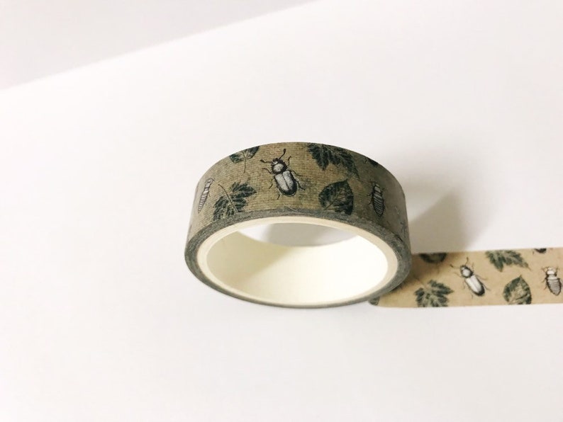 May include: A roll of brown washi tape with a repeating pattern of green leaves and black beetles.