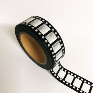 May include: A roll of black and white washi tape with a film strip design. The tape is on a white background.