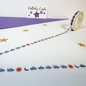 May include: A roll of decorative washi tape featuring a weather pattern of suns, clouds, moons, and lightning bolts. The tape is white with blue, red, and yellow designs. The image also includes a card with the text "Callaby Crafts".