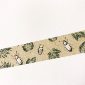 May include: A beige washi tape with a repeating pattern of green leaves and white and gray beetles.