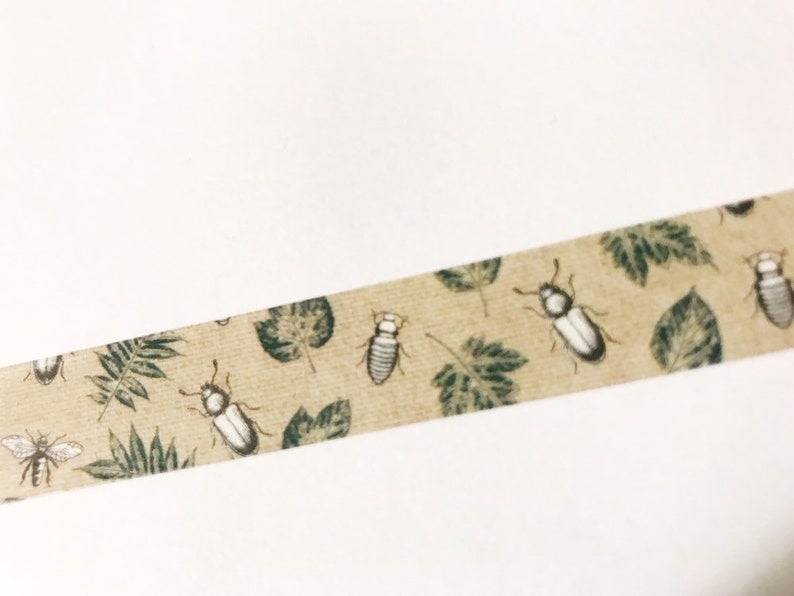 May include: A beige washi tape with a repeating pattern of green leaves and white and gray beetles.