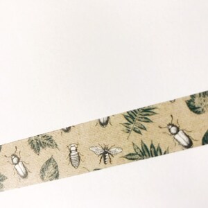 May include: A beige washi tape with a repeating pattern of green leaves and black and white insects.