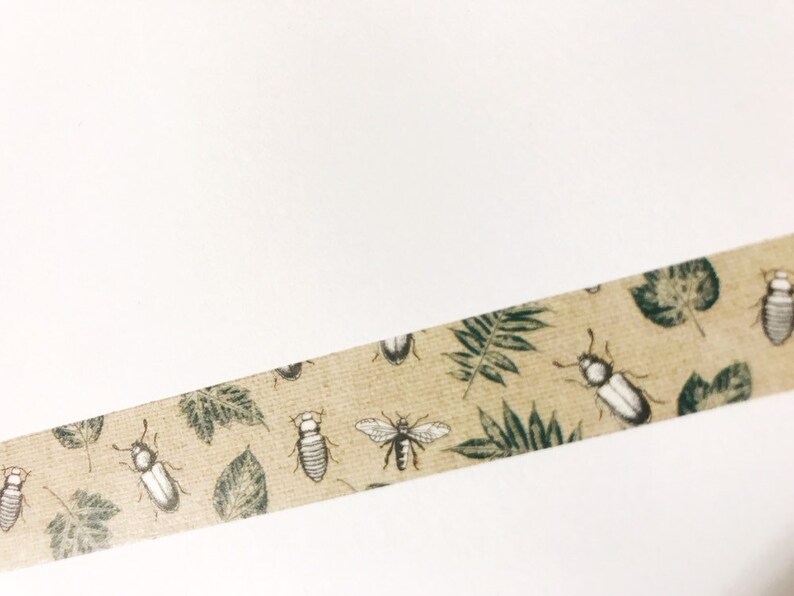 May include: A beige washi tape with a repeating pattern of green leaves and black and white insects.