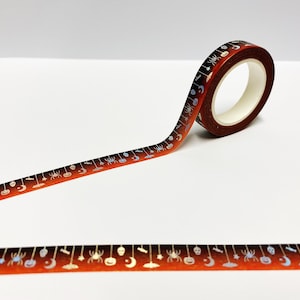 Op de afbeelding: Een rol Halloween washi tape met een oranje en bruine gradi&euml;nt achtergrond. De tape heeft zilveren illustraties van spinnen, pompoenen, manen en andere griezelige elementen. De tape is afgerold en toont het herhalende patroon.