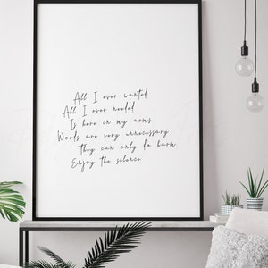 Op de afbeelding: Een ingelijste print met de tekst "All I ever wanted, All I ever needed, Is here in my arms, Words are very unnecessary, They can only do harm, Enjoy the silence." De print wordt weergegeven in een woonkamer met lichtroze stoelen en een ronde tafel.