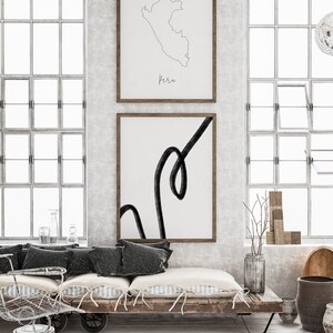 May include: Two framed art prints on a wall. The top print is a line drawing of Peru with the name "Peru" below. The bottom print features a black abstract line on a white background. The room has large windows.