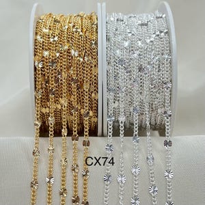 May include: Two spools of chain, one gold and one silver, with a decorative starburst pattern. The chain is on a white background. The text "CX74" is visible in the image.