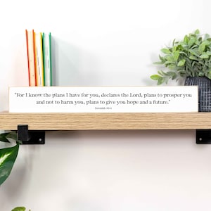 May include: White wooden sign with a gold border, featuring a bible verse from Jeremiah 29:11. The verse reads "For I know the plans I have for you, declares the Lord, plans to prosper you and not to harm you, plans to give you hope and a future."