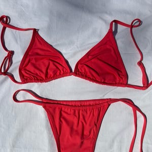 May include: A bright red bikini set with a triangle top and a high-cut bottom with tie sides.