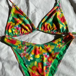 Peut inclure: Un haut et un bas de bikini à imprimé floral vert, jaune et rouge. Le haut du bikini est de style triangle et le bas est de style taille haute.