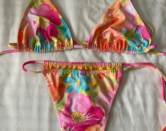May include: A floral print bikini with a triangle top and a high-cut bottom. The bikini is in shades of pink, orange, yellow, and blue.
