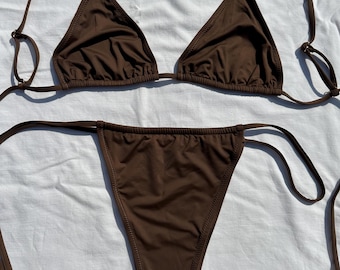 May include: A brown bikini set with triangle top and string tie bottoms. The swimwear is made of a smooth, solid-colored fabric. The top has adjustable straps, and the bottoms are a classic cut.