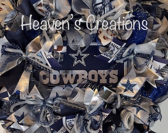 May include: A Dallas Cowboys wreath featuring blue, silver and white ribbons, mesh and a sign that reads "COWBOYS".