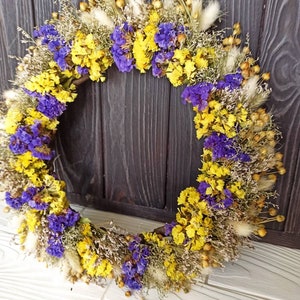 Peut inclure: Une couronne de fleurs séchées avec des fleurs jaunes et violettes, et des herbes séchées.