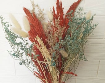 May include: A bouquet of dried flowers in shades of red, white, and blue. The bouquet includes pampas grass, bunny tails, and other dried foliage.