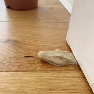 May include: A beige alligator-shaped doorstop with a textured surface. The doorstop is positioned under a white door.