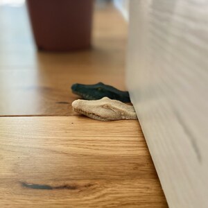 May include: Two alligator head doorstops, one green and one beige, are placed at the bottom of a white door.