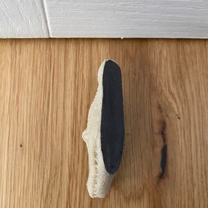 May include: A white doorstop with a black rubber backing. The doorstop is shaped like a shoe.