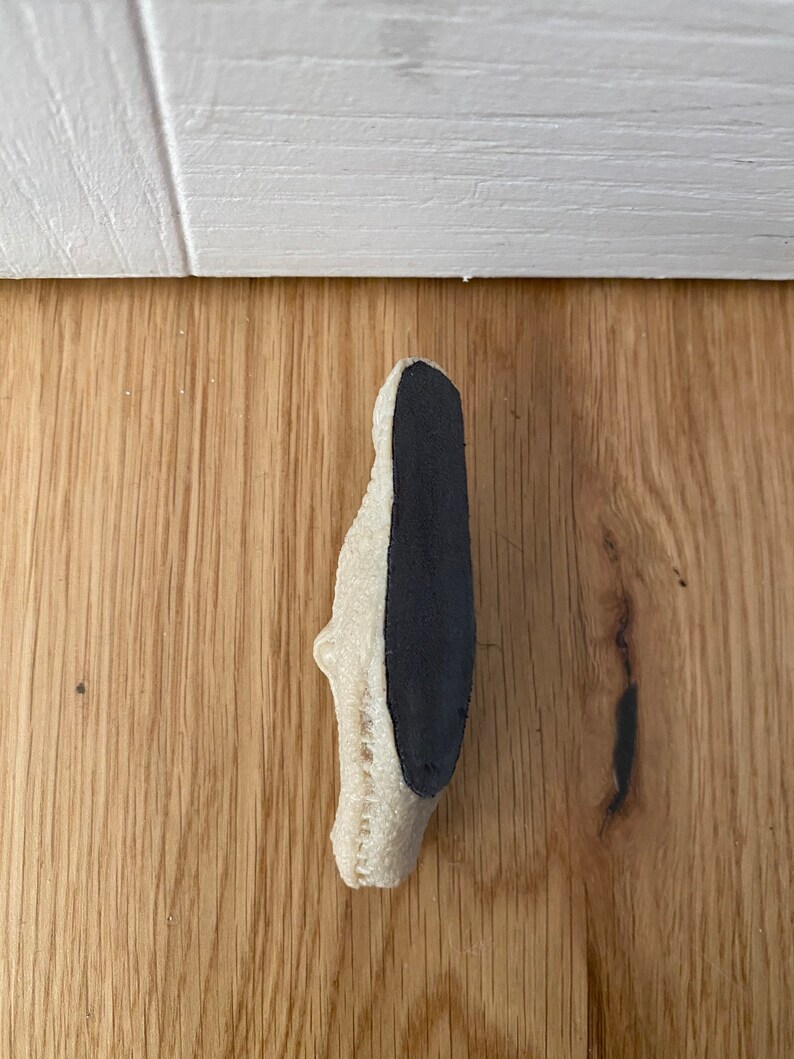 May include: A white doorstop with a black rubber backing. The doorstop is shaped like a shoe.