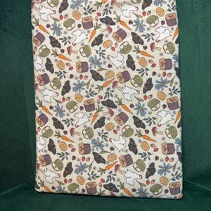 May include: A rectangular fabric cover featuring a cream-colored background with a repeating pattern of white chickens, orange carrots, blue flowers, brown butterflies, red mushrooms, and small jars. The top edge has a blue and white gingham trim.