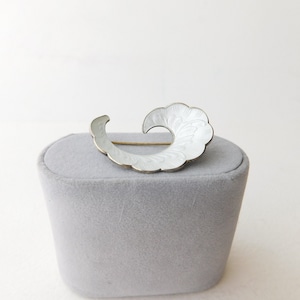 May include: A white enamel and sterling silver brooch in the shape of a swirl. The brooch has a delicate floral design.
