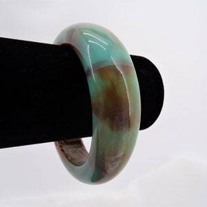 May include: A green and brown bangle bracelet made of polished stone. The bracelet is smooth and has a glossy finish.