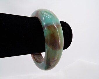 May include: A green and brown bangle bracelet made of polished stone. The bracelet is smooth and has a glossy finish.