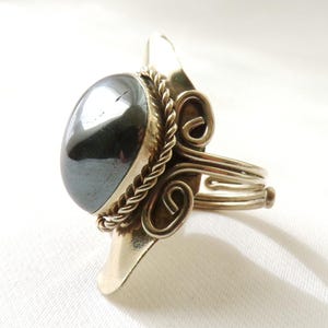 May include: A silver ring with a large, round, black hematite stone set in a decorative, twisted silver band.