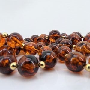 May include: A long strand of brown glass beads with a marbled effect. The beads are connected with gold-toned spacers.