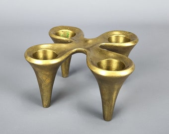 以下が含まれることがあります： 4つのキャンドルカップと3本の脚が付いた金色の金属製のキャンドルホルダー。キャンドルホルダーはモダンなスタイルでデザインされています。
