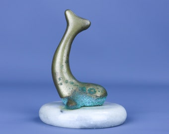 May include: A small, green bronze sculpture of a whale on a white marble base.