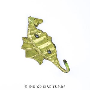 May include: A brass seahorse hook with a green patina. The hook is shaped like a seahorse with a curled tail and has three holes in the body.  The hook is on a white background.