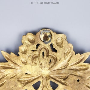 Puede incluir: Una pieza decorativa de metal dorado con un dise&ntilde;o floral. La pieza tiene un centro circular con un dise&ntilde;o en relieve y est&aacute; rodeada de hojas y flores.