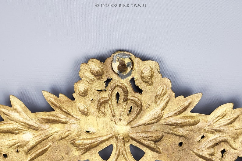 Puede incluir: Una pieza decorativa de metal dorado con un dise&ntilde;o floral. La pieza tiene un centro circular con un dise&ntilde;o en relieve y est&aacute; rodeada de hojas y flores.