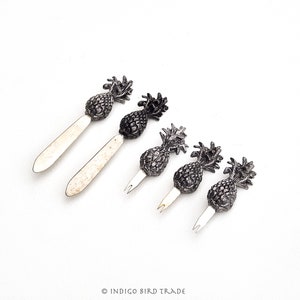 May include: Set of five silver pineapple cocktail picks. The picks are made of metal and have a pineapple design. They are perfect for adding a touch of fun to your next party.