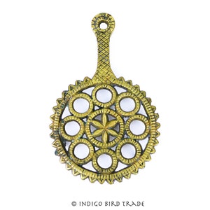May include: A gold-toned metal trivet with a circular design featuring multiple concentric circles and a starburst pattern in the center. The trivet has a handle for easy lifting.