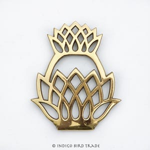 May include: A gold metal trivet in the shape of a stylized thistle. The trivet has a decorative, openwork design.