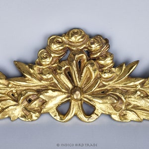Puede incluir: Una moldura decorativa de metal dorado con un dise&ntilde;o floral. La moldura presenta una roseta central rodeada de un grupo de rosetas m&aacute;s peque&ntilde;as. La moldura est&aacute; adornada con intrincados detalles de hojas.
