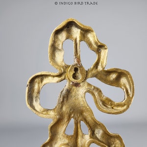 May include: Gold metal decorative wall hook in the shape of a stylized flower with a keyhole on the back.