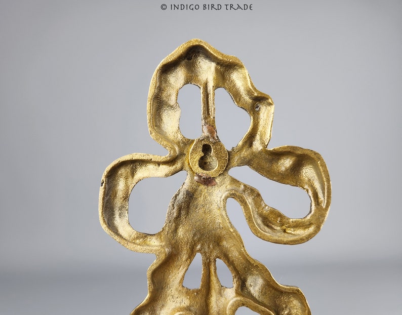 May include: Gold metal decorative wall hook in the shape of a stylized flower with a keyhole on the back.