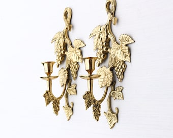 May include: A pair of gold-tone metal wall sconces with a grapevine design. Each sconce has two candle holders.