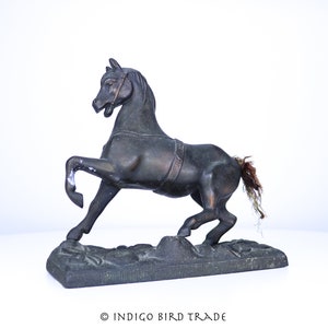 Peut inclure: Une statue de cheval en métal noir avec une patte avant levée et une longue queue. Le cheval est debout sur une base texturée.