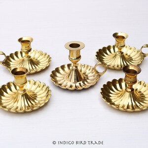May include: Set of five gold-toned brass candle holders. Four of the holders have a scalloped base with a handle and a single candle cup. The fifth holder has a single candle cup and a round base with a scalloped design.